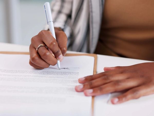 Person signing a document with a white pen on a clipboard.