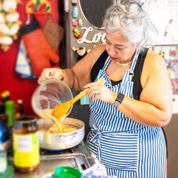 Mujer cocinando con delantal a rayas en una cocina colorida.