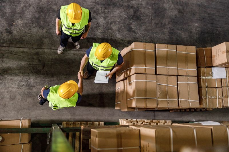 High angle view of two workers shaking hands while working with their colleague in distribution warehouse. Copy space.