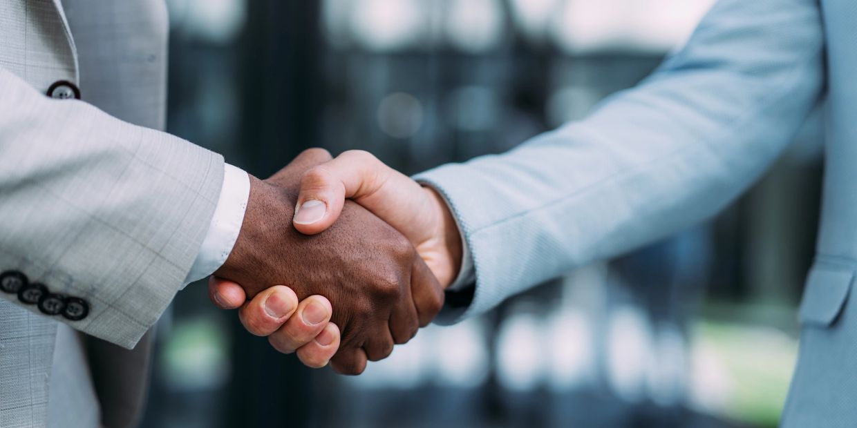 Two people in suits shaking hands in a professional setting.