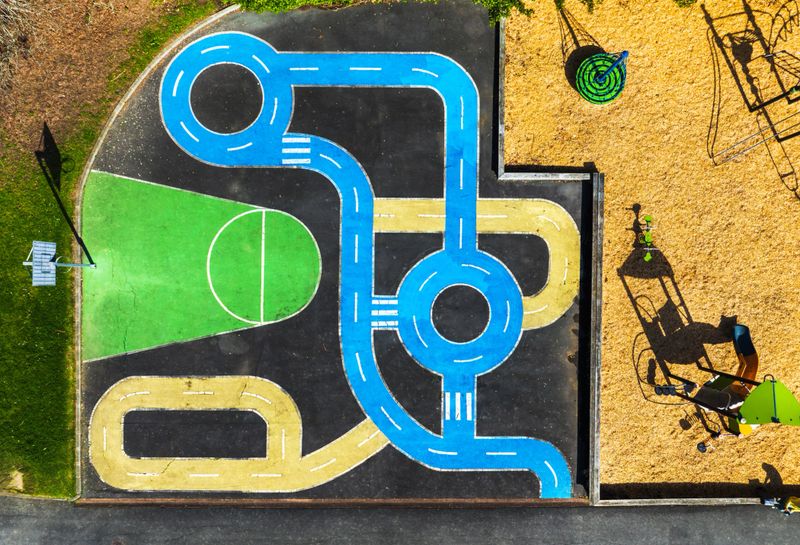 Aerial view of a colorful playground with a painted road track, slides, and a green area for basketball.
