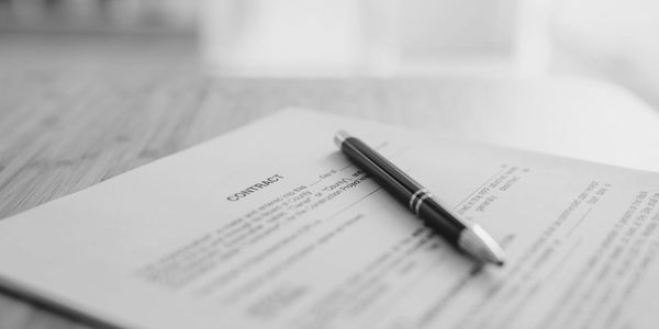 A document with the title "contract" laying on a table, accompanied by a pen.