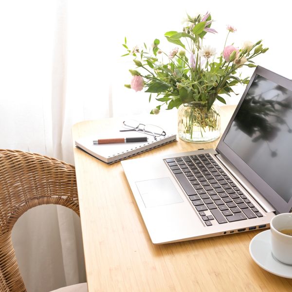 A cozy workspace with a laptop, notebook, flowers, and coffee on a wooden table.