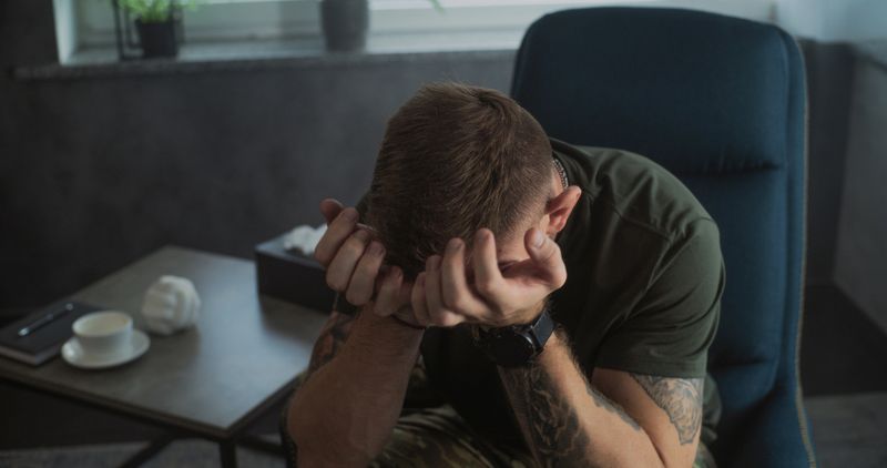 Male soldier talks to psychotherapist or psychologist, shares feelings. Portrait of stressed military man with PTSD crying during psychotherapy session. Post traumatic stress disorder. Mental health.