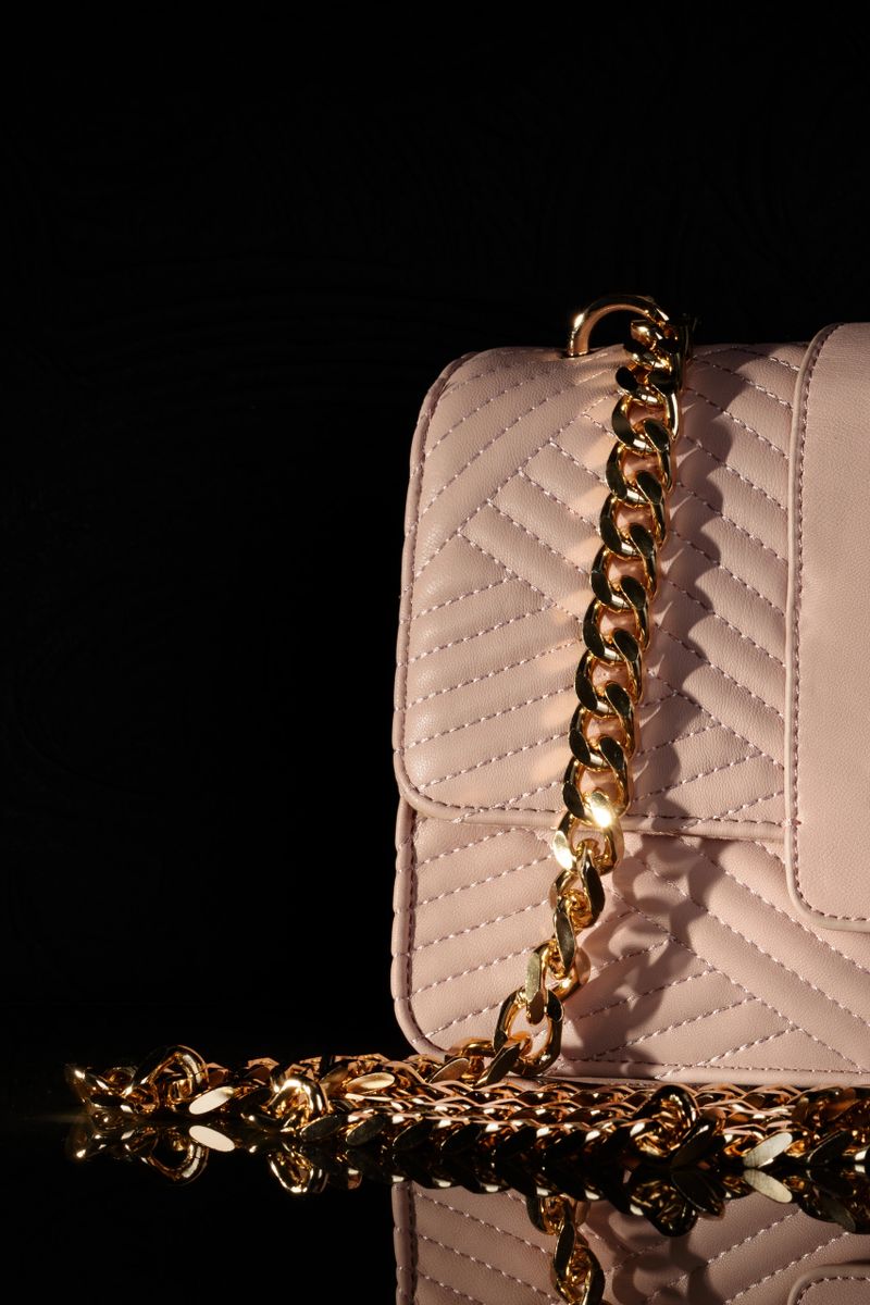 Elegant pink quilted purse with a gold chain strap, set against a black background.