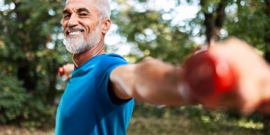 Older man exercising with red dumbbells outdoors.