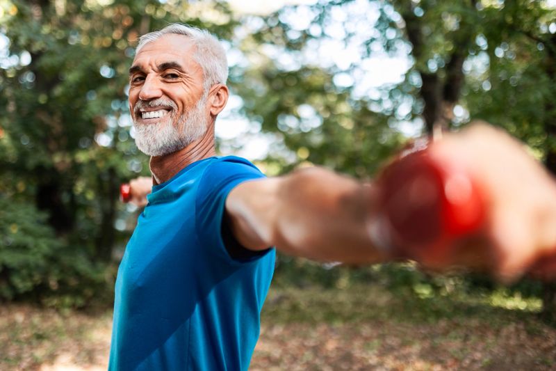 Senior man exercising with weights outdoors in park