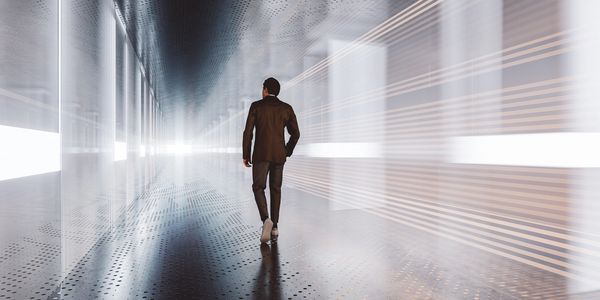 Man in suit walks through futuristic lit corridor with reflections.