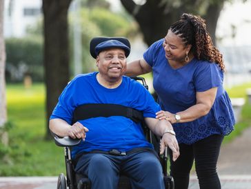 A woman happily pushes a man in a wheelchair outdoors.