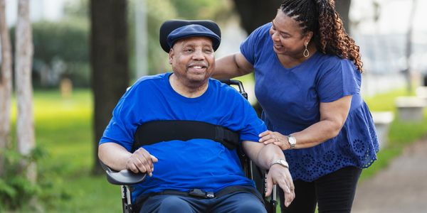 Woman caring for a man in a wheelchair outdoors.