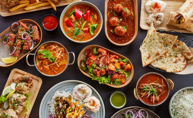 A diverse selection of delicious Indian dishes including curries, appetizers, naan bread, and various sauces arranged on a table