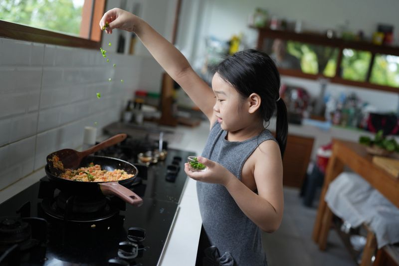 Little cute girl put ingredients in the pan, Cheerful Asian little girl cooking fried rice menu in the kitchen, improve skills for child