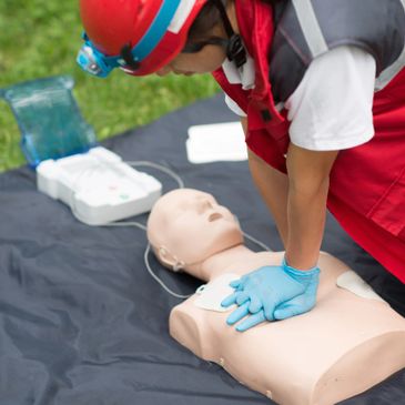 Person performing CPR on a training mannequin outdoors.