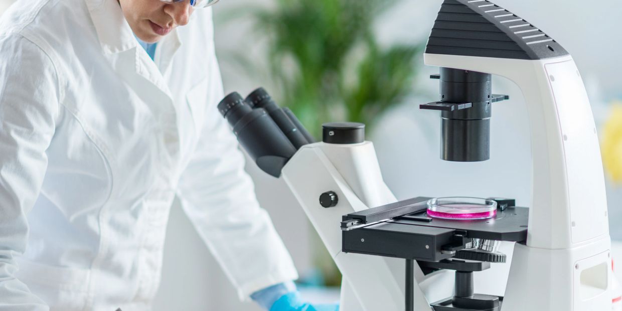 Scientist in protective gear working with a microscope and taking notes in a lab.