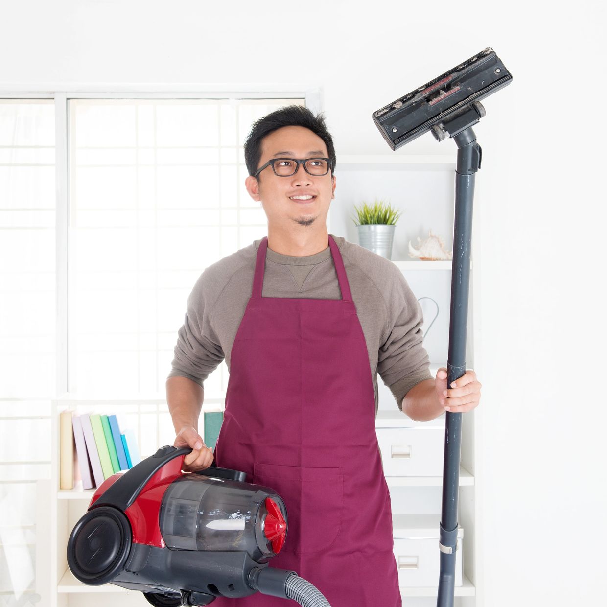 Man in apron holding a vacuum cleaner smiling indoors.