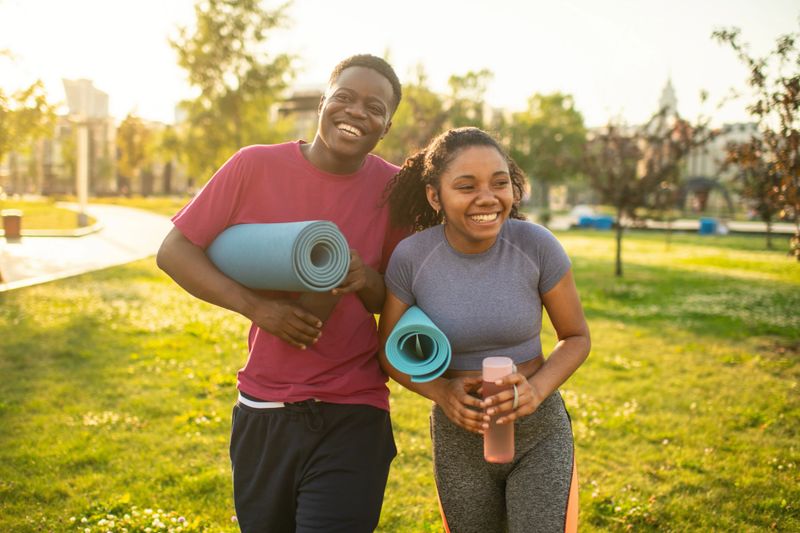Young couple with exercise mats walking in a summer park to practice yoga