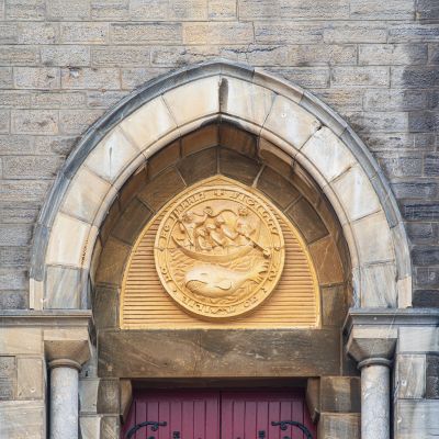 Stone archway with a circular emblem above a red door.