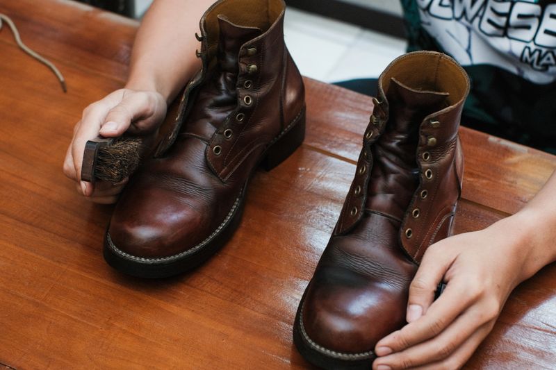 Close up of a hands polishing a leather boots with brush, on wooden table, shoes shining and cleaning.