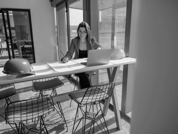 Woman working at a table with blueprints and laptop.