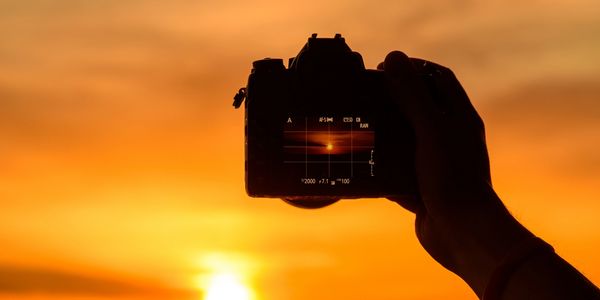 Silhouette of a hand holding a camera capturing a vibrant sunset.