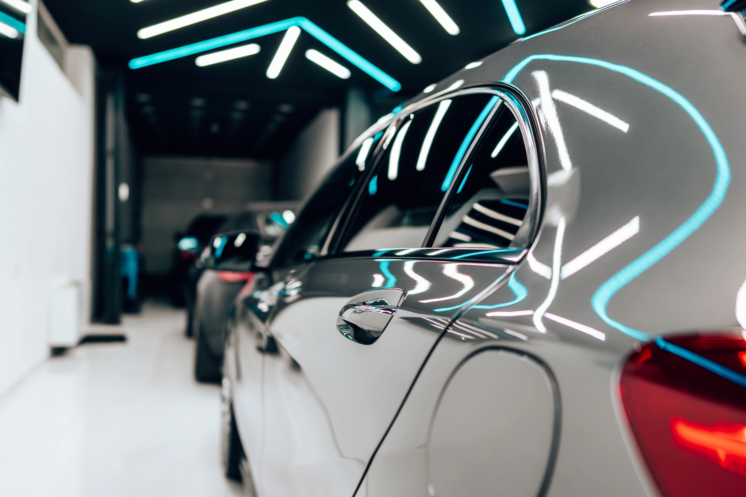 A sleek black car reflecting neon lights in a showroom. with our auto detailing services