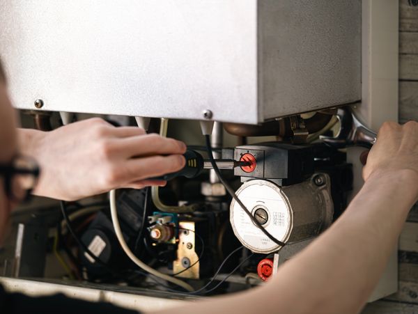 Technician repairing a boiler using tools.