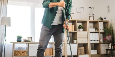 Man sweeping broken ceramic pieces on the floor in a cozy living room.