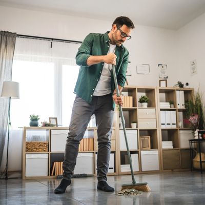 Man sweeping broken pieces from the floor inside a well-lit living room.