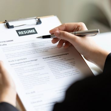 Person reviewing a resume with a pen in hand, focused on work experience.
