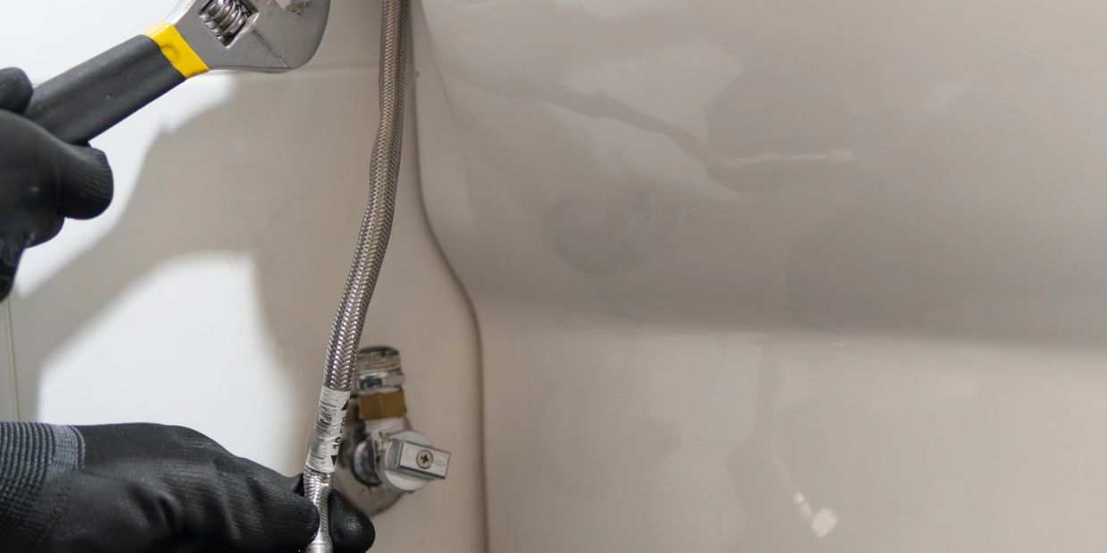 A person using a wrench to fix plumbing under a sink.