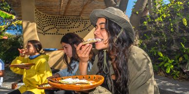 Three women enjoying traditional food outdoors on a sunny day.
