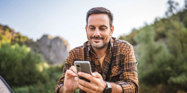 Middle-aged man using his phone outside with trees behind him.
