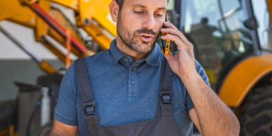 Construction worker talking on phone near heavy machinery.