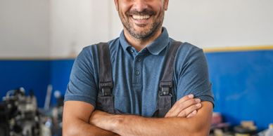 Smiling mechanic with arms crossed in workshop.