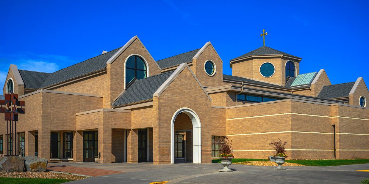 Modern brick church building with a golden cross on top under a clear blue sky.