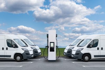 White electric vans parked on either side of a charging station under a blue sky.