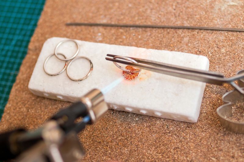 Detailed process of jewelry making with a torch on a white work surface in a creative studio.