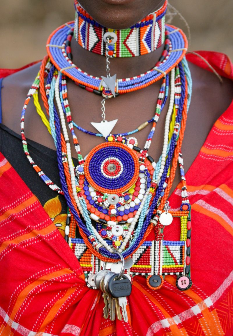 A Masai woman wearing her vibrantly colourful marriage beads including keys, neck collar, necklaces, buttons and metals shapes. Abstract colourful, eye catching splash of adornment. Amboseli, Kenya. No face. Full frame, close up.