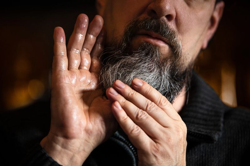 Grey bearded man applying beard oil or serum, care treatment at morning routine, men lifestyle