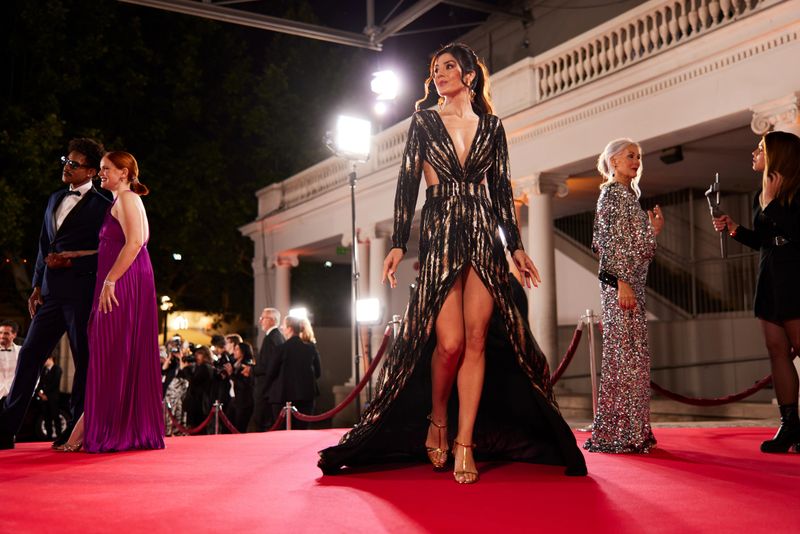 A stunning actress exits the interview area, a low-angle view capturing movie stars answering reporters in the background.