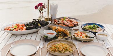 A seafood feast with shrimp, mussels, crab, and fish on a white outdoor table by the water.