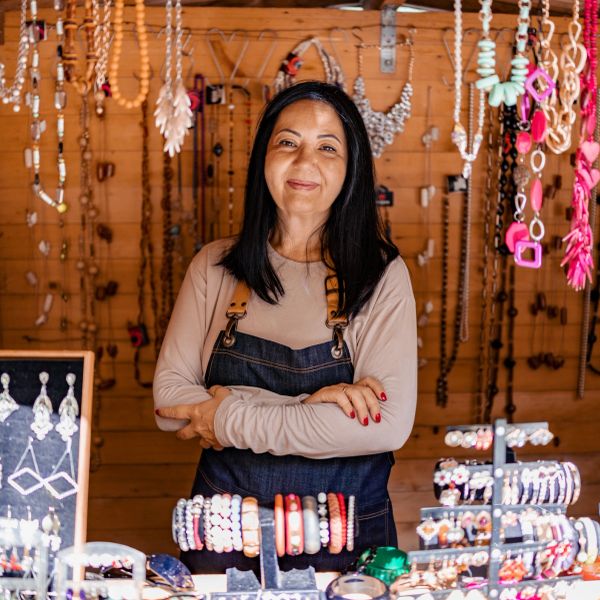 Smiling woman stands behind a jewelry display in a wooden shop.