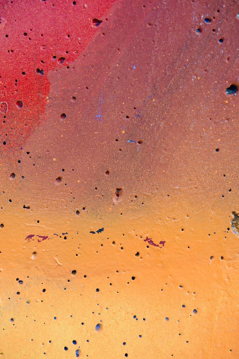 A close-up of an abstract surface featuring bold orange and red brushstrokes. The image highlights the textured patterns and dynamic movement within the strokes, creating a vibrant and visually engaging composition.