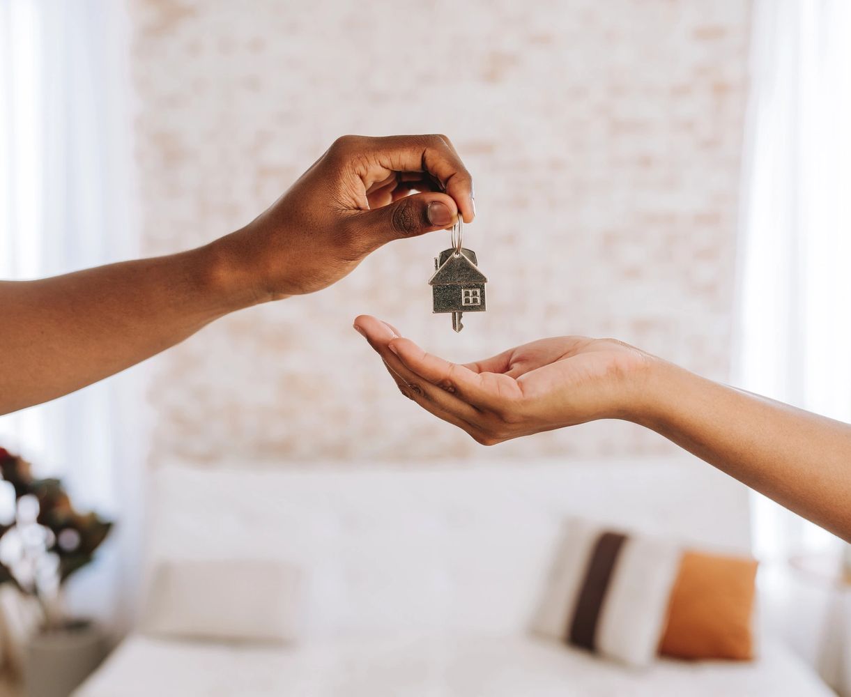 Two hands exchanging a house-shaped key in a cozy home setting.