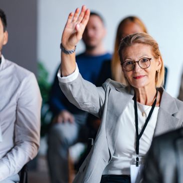 Woman in glasses raising her hand in a meeting or seminar.