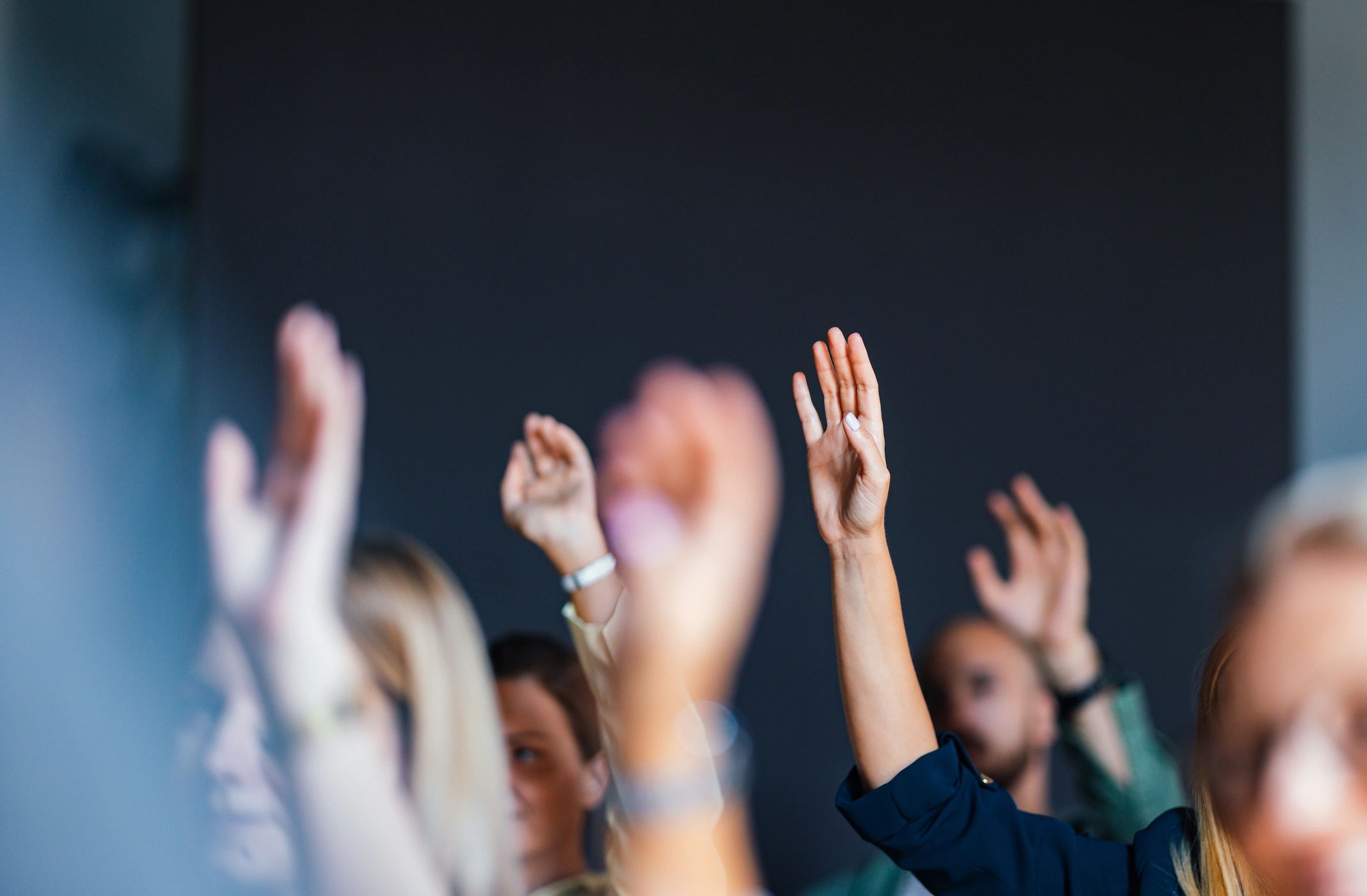 People raising hands in a meeting or classroom setting.