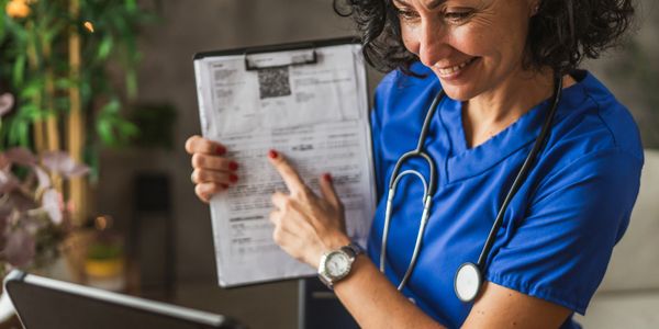Smiling nurse in blue scrubs showing a document on a clipboard.