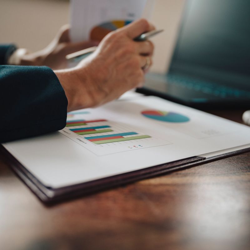 Low angle view of female hands holding paperwork with statistical financial report on it with graphs and charts. Business finance, profit and budgeting conceptual image.