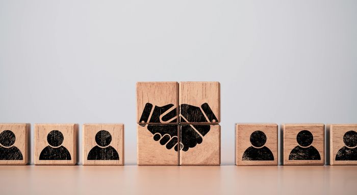 Wooden blocks showing handshake and people icons symbolizing partnership and teamwork.
