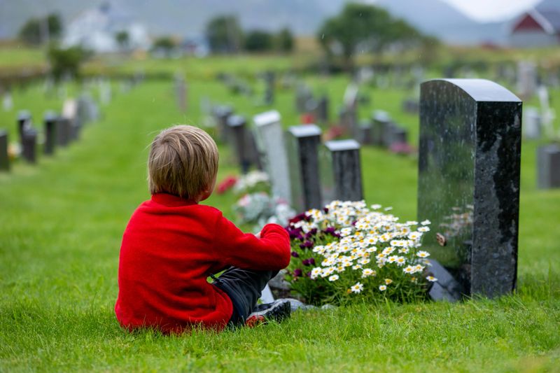 Sad little child, blond boy, standing in the rain on cemetery, sad person, mourning, summer rainy day